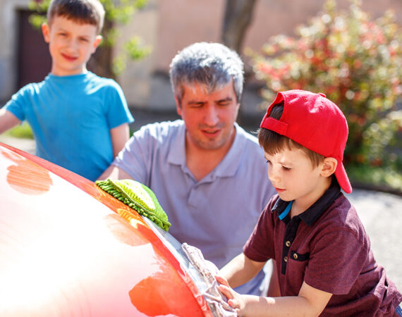 Family car wash, men at work. Little boy in cap cleaning the headlight