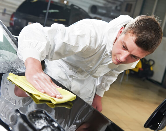 Auto mechanic worker polishing car bonnet with wiper at automobile repair and renew service station shop